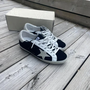 Golden Goose Superstar sneakers  - Golden Goose Superstar sneakers i svart och vitt med den ikoniska stjärndetalj på sidan. Ovandelen är i mocka och skinn, med grå mockadetaljer på hälen. Säljes med originalkartong, dustbag och certifikat. 