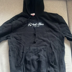 Svart hoodie från Mitchell & Ness - Svart hoodie från Mitchell & Ness med vit logga på bröstet. Storlek L