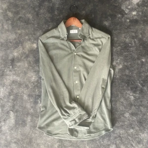 Grön skjorta från These Glory Days - Snygg grön skjorta från These Glory Days i slim fit-modell. Skjortan har långa ärmar och klassisk krage med knappar framtill. Perfekt för dig som gillar stilrena och enkla plagg.