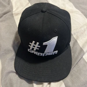 Svart keps med brodyr #1 GRIPPER - Svart keps med rak skärm och broderad text '#1 GRIPPER' i vitt framtill. Baksidan har texten 'MADE FOR CHAMPIONS BY CHAMPIONS'. Justerbar passform och signerad av frogfmx, jonathan karlsson, sibbe eriksson aldrig använd bara legat i låda 