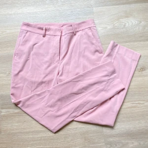 Ljusrosa kostymbyxor från KappAhl - Säljer ett par ljusrosa kostymbyxor från KappAhl i klassisk modell. Byxorna har hällor för bälte, diskreta bakfickor och stängs med hake och dragkedja. Perfekta för dig som vill ha en stilren och färgglad look. Liten fläck på vänster ben, se bild