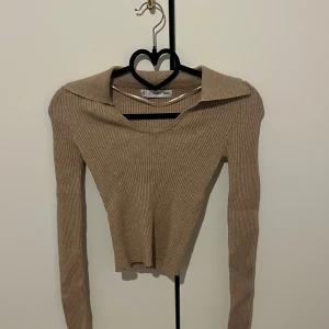 Beige ribbad långärmad topp från MNG - Säljer en beige ribbad långärmad topp från MNG. Tröjan har en unik krage med knappdetalj och är croppad i modellen. Perfekt för dig som gillar stilrena och trendiga plagg.