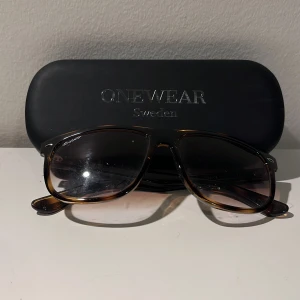 Bruna solglasögon från Onewear Sweden - Snygga solglasögon från Onewear Sweden med brunt, lätt transparent båge och mörka glas. Klassisk rektangulär form som passar de flesta ansikten. Kommer med originalfodral och tygpåse med logga.