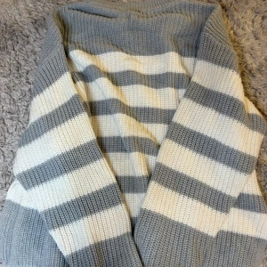 Gråvit randig stickad kofta - Mysig stickad kofta med breda grå och vita ränder. Koftan har lång ärm och är perfekt för lager-på-lager-stil. Tjockt och mjukt material som håller dig varm under kyliga dagar.