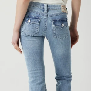 Ljusblå jeansbyxor från True Religion - Säljer ett par ljusblå jeansbyxor från True Religion med klassiska bakfickor och dekorativa sömmar. Byxorna har normal passform och raka ben. Perfekta för en avslappnad stil. Har använts 2 gånger och dom var för lågmidjade och långa för min smak så väljer att sälja dom, Storlek 24 kom privat för snabb diskussion av pris eller fler bilder. 