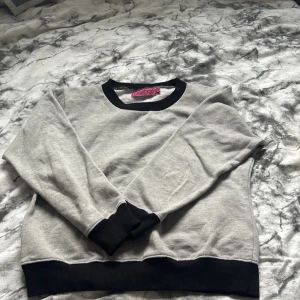 Grå sweatshirt med svarta detaljer från Boohoo - En stilren grå sweatshirt från Boohoo med svarta muddar vid hals, ärmslut och nederkant. Tröjan har en klassisk passform och är perfekt för en avslappnad look. Mjuk och bekväm, passar till många tillfällen.