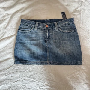 Blå jeanskjol med fickor kort och lowwaist - Midjemått 36cm längd 31cm Säljer en klassisk blå jeanskjol i minilängd med fem fickor och bälteshällor. Kjolen har en knapp och dragkedja framtill samt två stora bakfickor. Perfekt till vardags med en enkel topp.