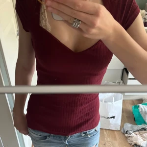 Vinröd ribbad topp från Anna Field - Säljer en vinröd ribbad topp från Anna Field med v-ringning och korta ärmar. Toppen har en tight passform och är tillverkad i mjuk bomullsmix. Perfekt att styla med jeans eller kjol. Nästan helt oanvänd utan synligt slitage