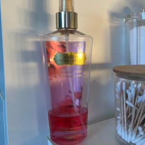 Victoria's Secret Mango Temptation Body Mist - En fruktig body mist från Victoria's Secret med doft av mango och hibiskus. Flaskan är genomskinlig med rosa vätska och har en guldfärgad spraypump och etikett. Perfekt för dig som gillar tropiska och söta dofter. Det är den orginala flaskan som inte går att få tag på längre!