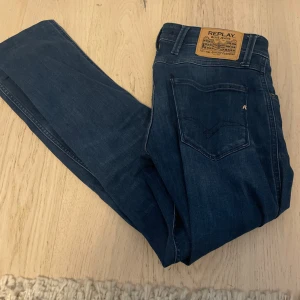 Mörkblå jeansbyxor från Replay - Säljer ett par mörkblå jeansbyxor från Replay med klassisk femficksdesign och läderpatch bak i midjan. Jeansen har raka ben och subtila slitningar framtill för en snygg vardagslook.