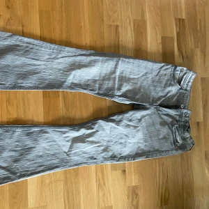 Grå jeansbyxor från H&M med broderade bakfickor - Säljer ett par grå jeansbyxor från H&M med justerbar midja och broderade detaljer på bakfickorna. Byxorna har klassisk femficksdesign och stängs med dragkedja och knapp. Perfekta för dig som gillar en enkel men snygg stil.