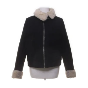 Svart jacka med fuskpäls - Säljer en svart jacka med beige fuskpäls på krage och ärmslut. Jackan har rak passform och stängs med dragkedja framtill. Perfekt för kyligare dagar och ger en cool look.