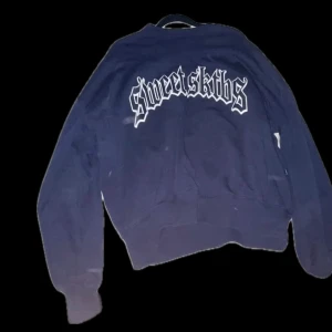 Mörk blå sweatshirt med tryck från Sweet SkTBS - Cool mörk blå sweatshirt med stort vitt tryck på bröstet från Sweet SkTBS. Tröjan har en klassisk passform och är perfekt för en avslappnad streetwear-look. Kostar ca 600-700