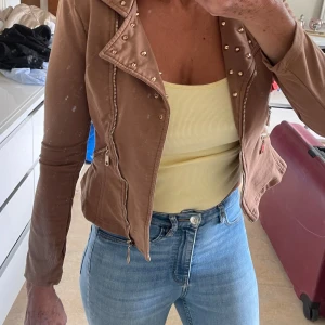 Brun bikerjacka med nitar från Drôle de Copine - Snygg brun bikerjacka frånDrôle de Copine med coola nitar på kragen och flera dragkedjor framtill. Jackan är croppad och har lång ärm, perfekt för dig som vill ha en edgy stil. Materialet känns mjukt och är töjbart.passar även i medium storlek .kan möta er i Stockholm city utanför Åhléns 