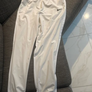 Straight/bredare vindbyxor Nike - Byxorna har rak passform och är tillverkade i ett lätt syntetmaterial, perfekta för sport eller avslappnade dagar. Knappt använda i storlek L