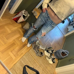Blå slitna jeans med hål - Kan diskutera priset Säljer ett par blå jeans med slitningar och stora hål på knäna. Byxorna har en rak passform och är i klassisk denim med fem fickor och dragkedja. Perfekta för en avslappnad och trendig look.