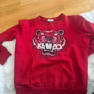 Röd sweatshirt med tiger från Kenzo - Säljer en röd sweatshirt från Kenzo med ikoniskt tigerbroderi och logga på bröstet. Tröjan har rund halsringning och långa ärmar. Perfekt statement-plagg för dig som gillar streetwear. Storlek S