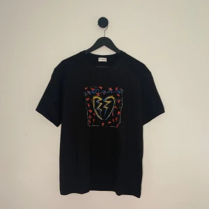 Saint Laurent T-shirt  - Svart t-shirt från Saint Laurent med färgglatt tryck framtill. Trycket har ett gult och blått hjärta med blixt och röda trianglar runtom, samt texten 'Saint Laurent' i blått. Klassisk passform och rund hals.