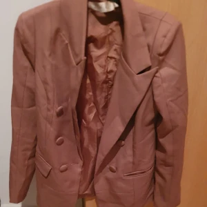 Kavaj - Säljer en stilren brun kavaj med breda slag och dubbelknäppning. Kavajen har långa ärmar och två framfickor med lock. Perfekt för en elegant look.