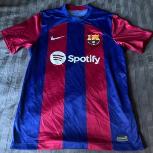 FC Barcelona t-shirt - Säljer en officiell FC Barcelona fotbollströja från Nike med Spotify som sponsor. Tröjan är blå och röd med breda vertikala ränder, klubbmärke på bröstet och UNHCR-logga på ryggen. Klassisk rund hals och korta ärmar. Köpt i Barcelona på el classico så den är 100% äkta. 