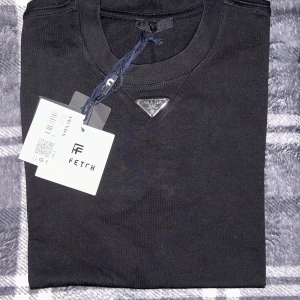 Svart sweatshirt från Prada - Säljer en svart sweatshirt från Prada med klassisk rund halsringning och den ikoniska metalltriangeln framtill. Tröjan är i mjuk bomull och har en stilren, minimalistisk design. Perfekt för dig som gillar exklusiva märken och enkel stil.