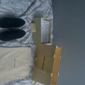 Svarta sneakers från Axel Arigato - Snygga svarta sneakers från Axel Arigato med vit sula och diskret logga på sidan. Perfekta för en stilren look. Skorna kommer med originalförpackning och påse.