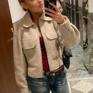 Beige teddyjacka med dragkedja - Säljer en snygg beige teddyjacka med dragkedja och stora fickor framtill. Jackan har en croppad passform och långa ärmar, i jättebra skick!