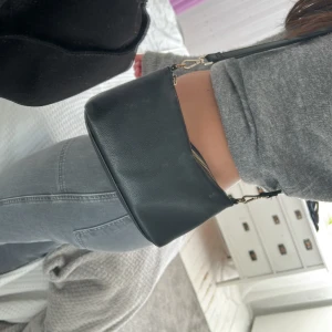Svart axelväska i skinn - Snygg svart axelväska i skinn med justerbar rem och dragkedja. Perfekt för att bära dina nödvändigheter med stil. Enkel och elegant design som passar till många olika outfits.