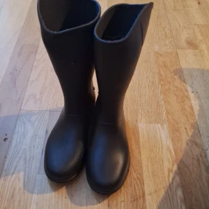 Svarta ridstövlar  - Säljer ett par klassiska svarta stövlar med rund tå. Perfekta för regniga dagar och håller fötterna torra. De har en enkel och stilren design som passar till det mesta.