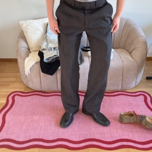 Kostymbyxor  - Snygga bruna kostymbyxor med pinstripes. Byxorna har en klassisk design med knappar och dragkedja framtill. Perfekta för en stilren look. Storlek 50 och raka i benet!