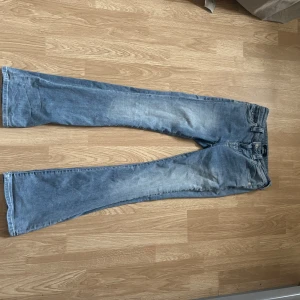 Blå jeans från True Religion - Snygga blå jeans från True Religion med klassisk femficksdesign och knappar på bakfickorna. De har en bootcut-stil och är perfekta för en avslappnad look. Märkeslogga på baksidan ger en extra touch.