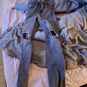 Grå jeans med slitningar från Zara - Säljer ett par grå jeans från Zara med coola slitningar på knäna. De har en klassisk femficksdesign och knappar i midjan. Storlek 34