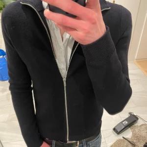 Svart cardigan jacka med dragkedja - Snygg mörk blå cardigan jacka med dragkedja framtill. Perfekt för lite kyligare sommarkvällar då man vill vara lite extra uppklädd. Passar superbra med en skjorta under som ett exempel! Tröjan är ifrån Brothers och är använd max 10 gånger, en liten defekt! På armen, men syns knappt om man inte kollar noga. Skriv vid fundering!