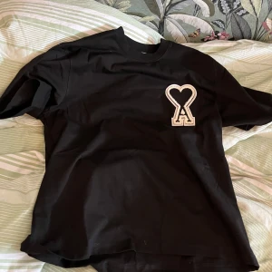 Svart t-shirt från AMI - Snygg svart t-shirt från AMI med ett unikt hjärtmönster på bröstet. Perfekt för en stilren look. Tillverkad i mjukt material för extra komfort.