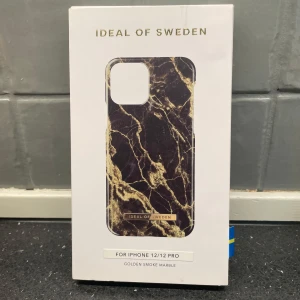 Mobilskal Golden Smoke Marble från iDeal of Sweden - Snyggt mobilskal från iDeal of Sweden i mönstret Golden Smoke Marble. Passar iPhone 12/12 Pro. Skalet har en elegant marmordesign i svart och guld som ger en lyxig känsla. Perfekt för att skydda din telefon med stil.