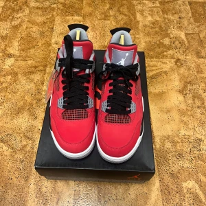 Röda Nike Air Jordans 4 toro bravo - Snygga röda Nike Air Jordans med svarta och grå detaljer. Skorna har en ikonisk design med snörning och vit sula. Perfekta för dig som vill ha en stilren och sportig look.