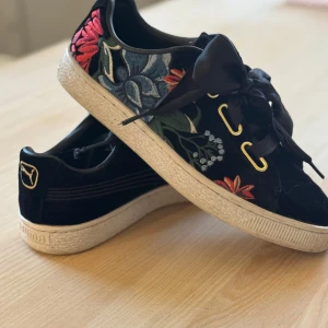 Puma sneakers  - Snygga svarta sneakers från Puma med färgglatt blommigt broderi på sidorna. Skorna har breda siden snören och fina guld detaljer.