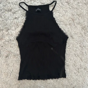 Svart ribbad linnetopp från even &odd - Snygg svart ribbad linnetopp med spetsdetaljer längs kanterna. Perfekt för en stilren look. Den har smala axelband och en hög halsringning.