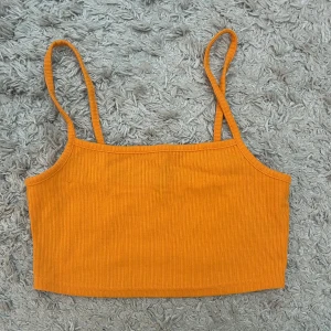 Orange ribbad linnetopp - Säljer en snygg orange ribbad linnetopp med smala axelband. Perfekt för varma sommardagar eller som ett lager under en jacka. Enkel och stilren design som passar till det mesta.