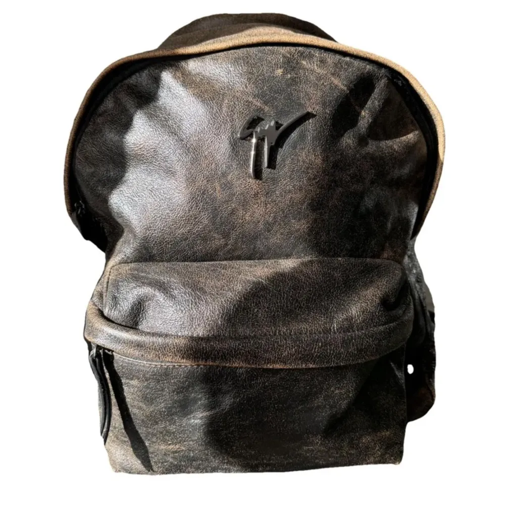 Snygg brun ryggsäck i skinn med ett stilrent märke på framsidan. Ryggsäcken har en praktisk dragkedja och en klassisk design som passar perfekt för vardagsbruk. Den har en rymlig huvudficka och en mindre ficka framtill för enkel åtkomst till dina saker.. Laukut & Käsilaukut.