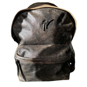 Brun ryggsäck i skinn - Snygg brun ryggsäck i skinn med ett stilrent märke på framsidan. Ryggsäcken har en praktisk dragkedja och en klassisk design som passar perfekt för vardagsbruk. Den har en rymlig huvudficka och en mindre ficka framtill för enkel åtkomst till dina saker.