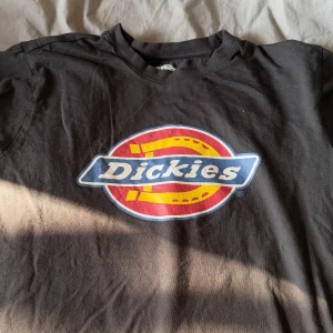 Svart t-shirt från Dickies - Säljer en svart t-shirt från Dickies med deras ikoniska logga i rött, gult och blått på framsidan. Perfekt för en avslappnad stil. T-shirten är kortärmad och gjord i bomull. Passar bra till jeans eller shorts!