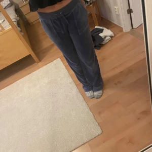 Juicy couture - Säljer ett par bekväma blå mjukisbyxor med snörning i midjan. Byxorna har en loose passform och är perfekta för en avslappnad stil. De har praktiska fickor både fram och bak. Störenas metallgrejer har åkt av, de är uppsydda för att passa mig som är 161 cm, färg greyblue
