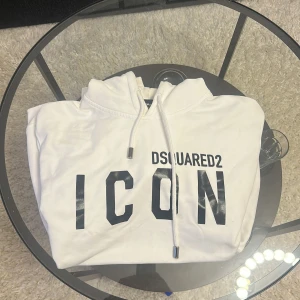 Vit hoodie från Dsquared2 - Liten i storlek är som en XL. Säljer en snygg vit hoodie från Dsquared2 med texten 'ICON' i svart på framsidan. Hoodien har en klassisk design med dragsko i huvan. Perfekt för en stilren och avslappnad look. 