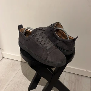 Grå sneakers från Christian Louboutin - Snygga grå sneakers i mocka från Christian Louboutin med den ikoniska röda sulan. Sulan är lite sliten vilket inte är konstigt då den är använd ett antal gånger, men väldigt bra skick generellt på skon.