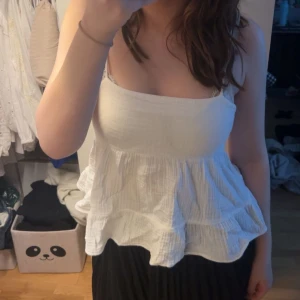 Vit ärmlös topp med volang - Säljer en söt vit ärmlös topp med volangdetaljer från gina tricot! Toppen har en knytning i ryggen och är väldigt söt!