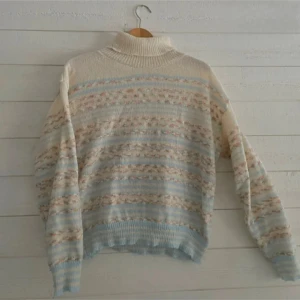 Mönstrad stickad polotröja i vårfärger - Säljer en mysig stickad polotröja med ett vackert mönster i ljusblått, beige och rosa. Tröjan har långa ärmar och en bekväm polokrage. Perfekt för kyliga sommar kvällar.