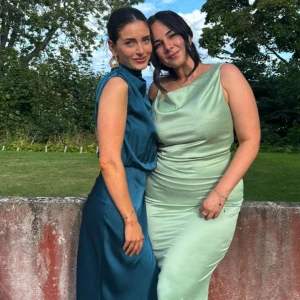 Blå axelbandslös klänning - Elegant blå axelbandslös klänning i satin med en draperad topp och lång kjol. Perfekt för festliga tillfällen.