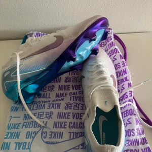 Nike Mercurial fotbollsskor - Snygga Nike Mercurial fotbollsskor i vitt med lila och blå detaljer. Helt nya skor använt dem en gång bara, men var för stora tyvärr. Storlek 44