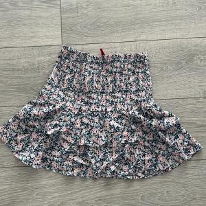 Blommig kjol från H&M Divided - Söt blommig kjol från H&M Divided i rosa och blå toner. Kjolen har en volangdetalj och en elastisk midja för en bekväm passform. Perfekt för en somrig look!